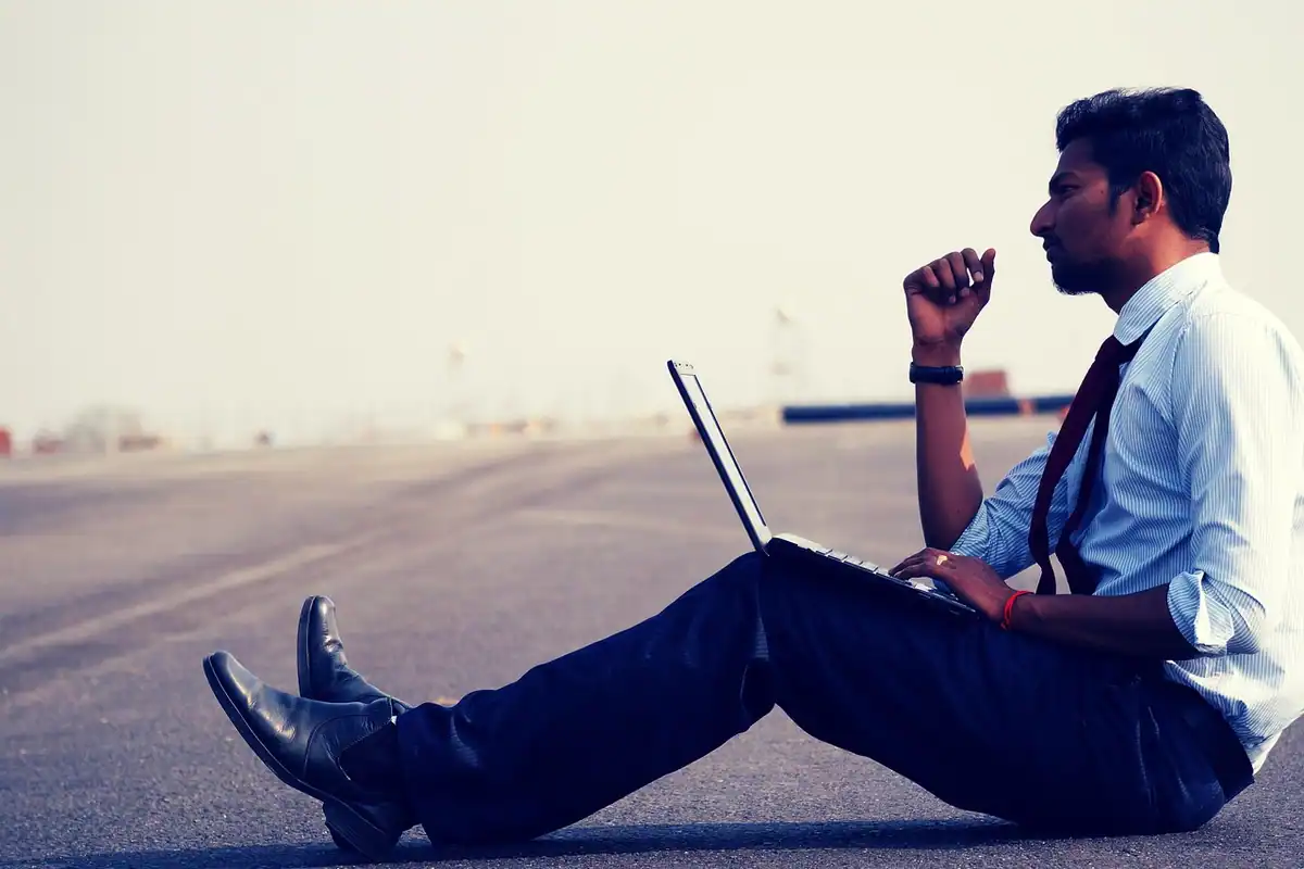 Freelancer așezat pe asfalt, cu laptopul pe genunchi, își calculează contribuția la pensie