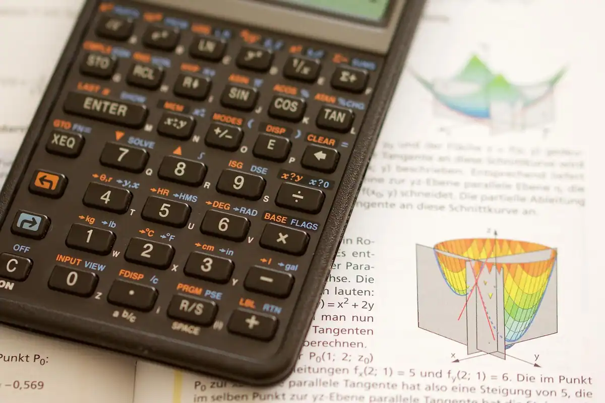 Calculator științific așezat peste o carte de matematică deschisă, pentru calculul bazei CAS