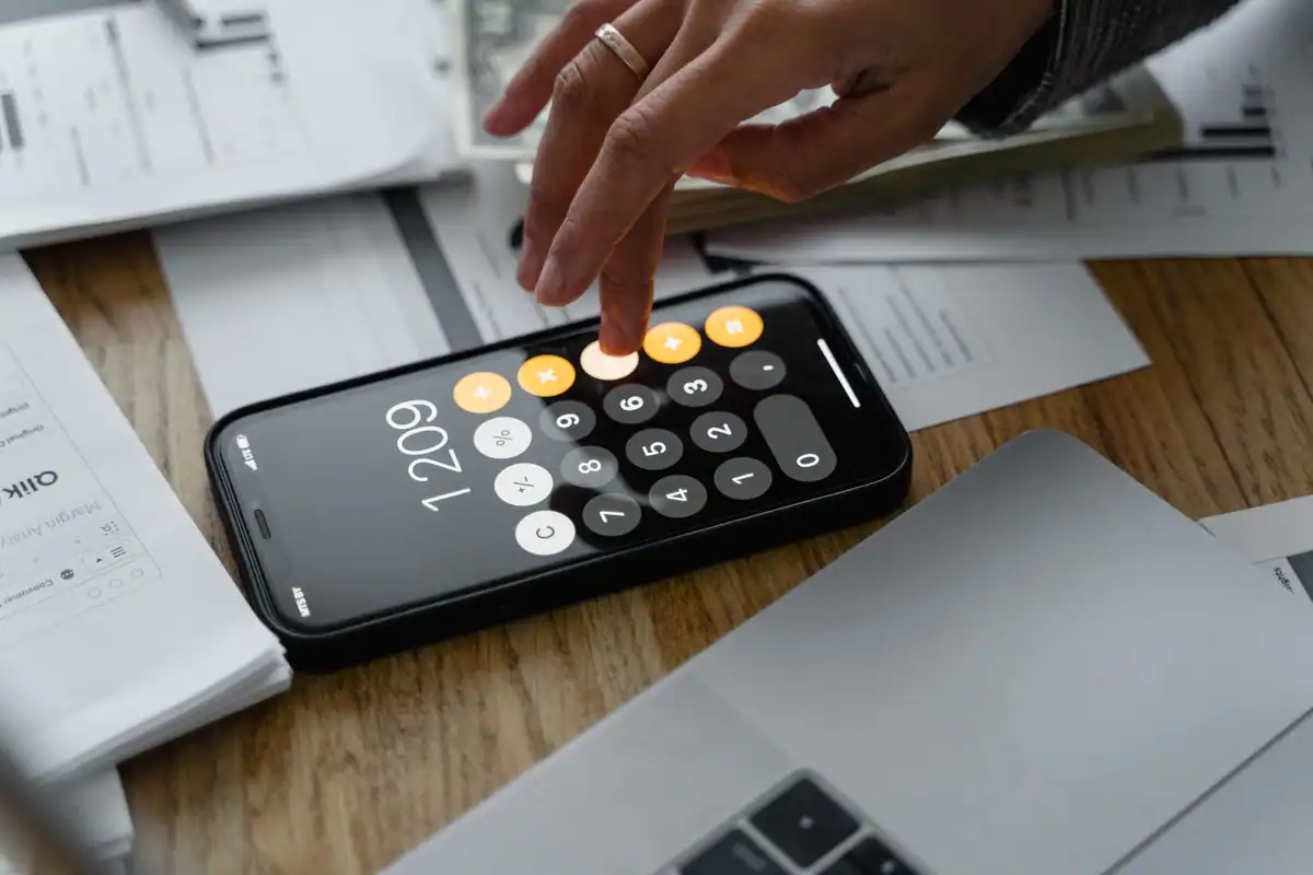 Mână care tastează pe calculatorul din telefon, deasupra unor documente despre venitul extrasalarial