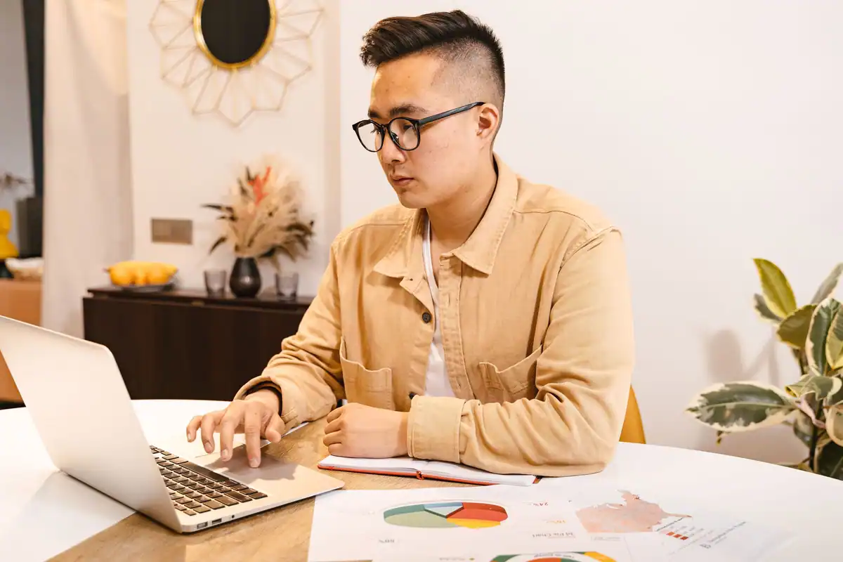 Bărbat cu ochelari care tastează pe laptop, la o masă luminoasă din sufragerie