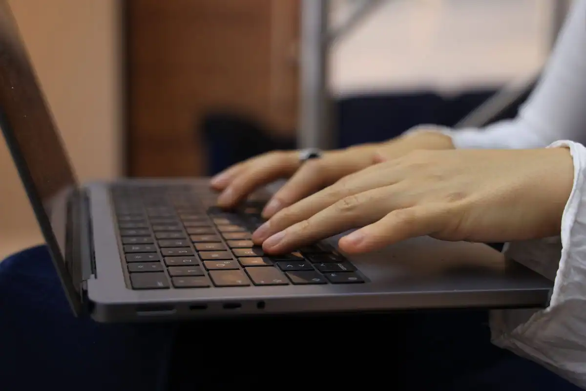 Mâini care tastează pe tastatura unui laptop, în timpul completării formularului online
