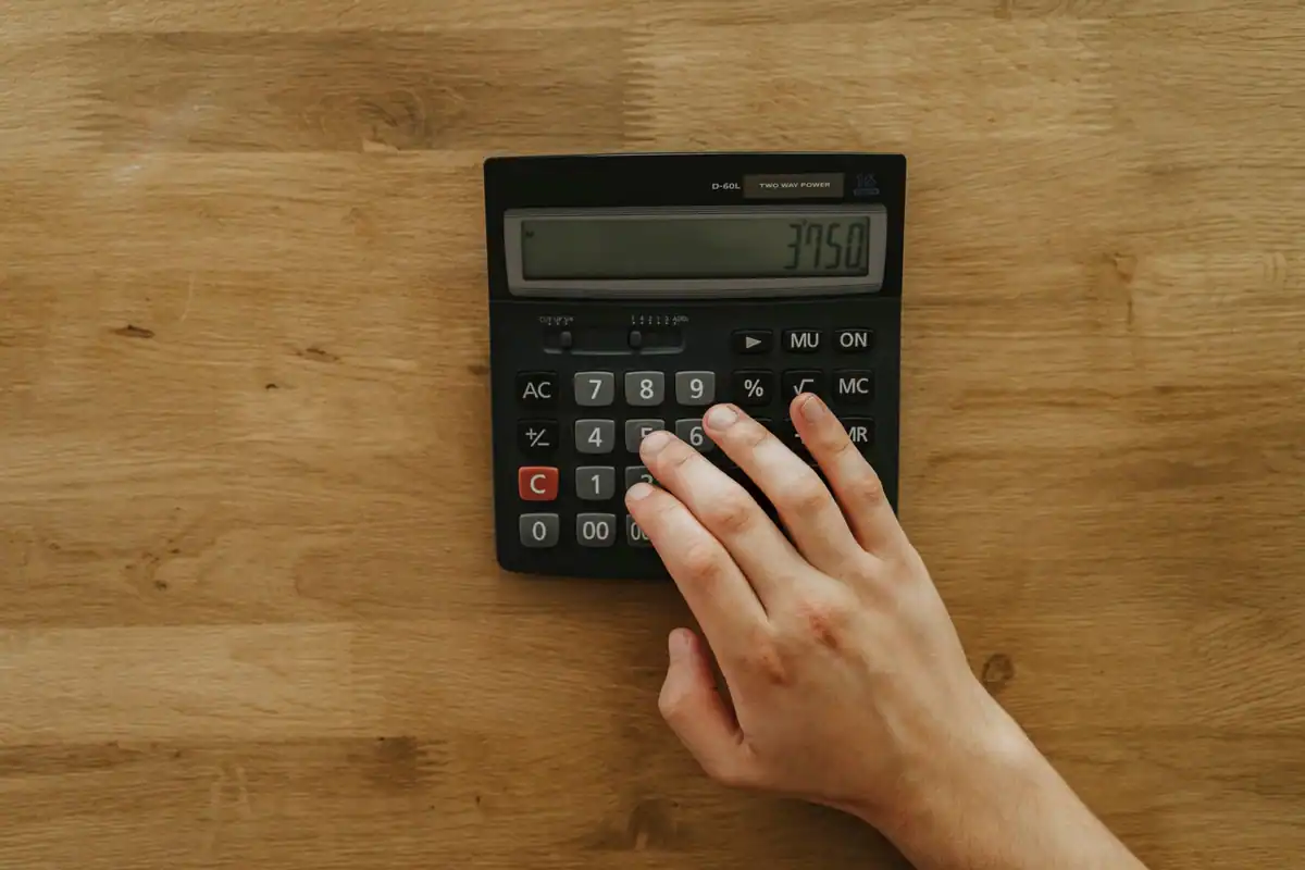 Mână care apasă pe un calculator așezat pe un birou din lemn, pentru contribuțiile din salariu