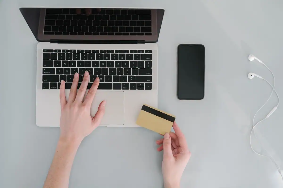 Mâini pe tastatura unui laptop și un card bancar auriu, la plata online