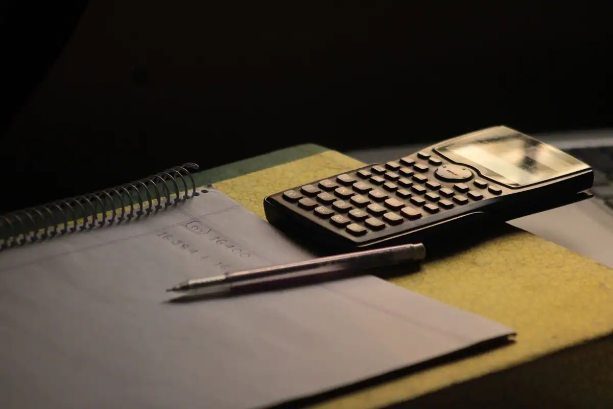 Calculator pe un caiet, cu un pix alături, într-o lumină caldă de birou