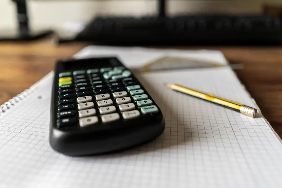 Calculator negru și creion galben pe un caiet cu pătrățele, pentru calculul dividendelor