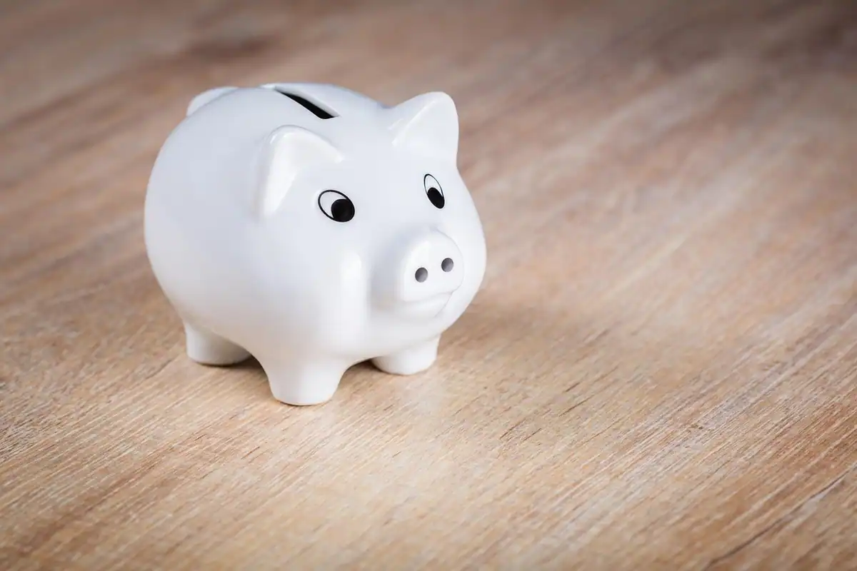 Pușculiță albă în formă de porc, pe o masă de lemn, pentru economiile de la bancă