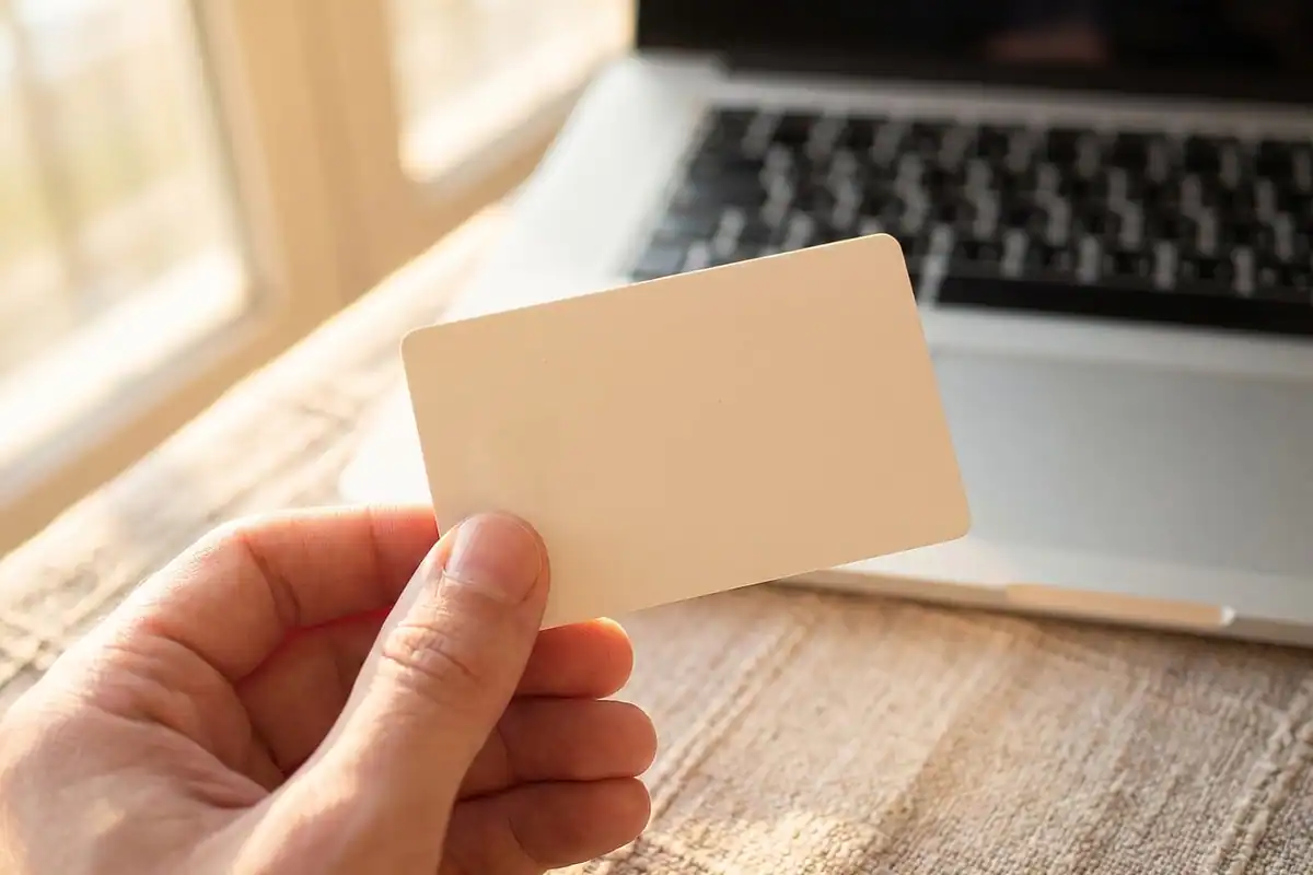 Mână care ține o carte de vizită goală lângă un laptop, pentru identificarea în SPV