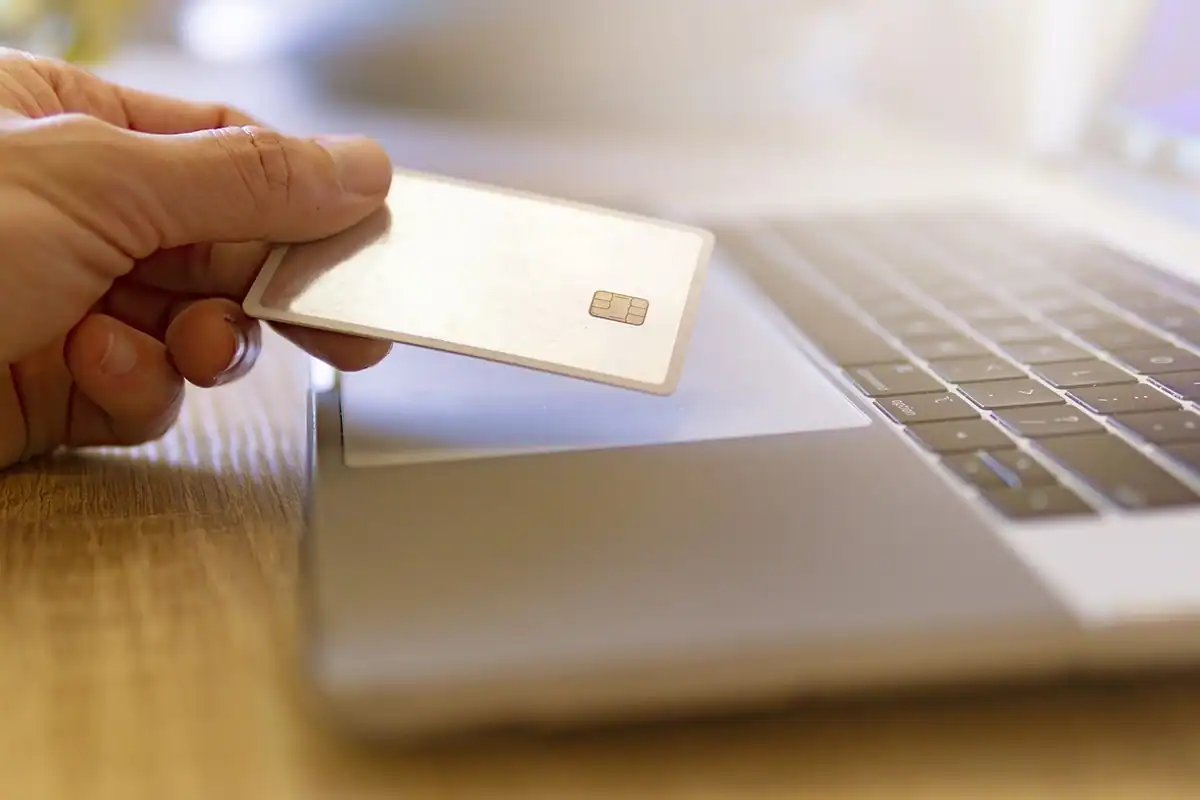 Mână care ține un card în dreptul unui laptop, la plata online a obligațiilor
