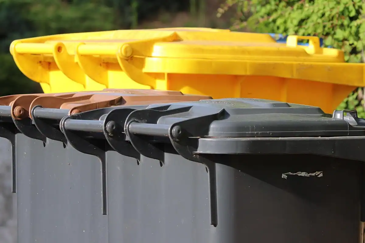 Containere negre cu capac galben pentru deșeuri menajere, așezate în rând