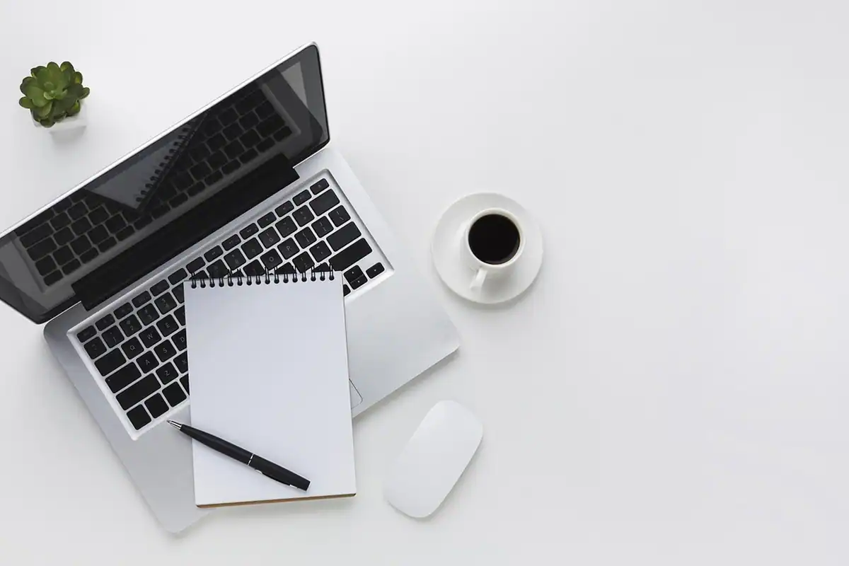 Laptop, caiet și o ceașcă de cafea, văzute de sus, pe o masă albă